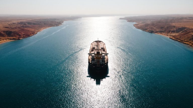Aerial view of Hormuz-like strait with lone tanker and $91 Brent crude marker — oil-driven inflation analysis