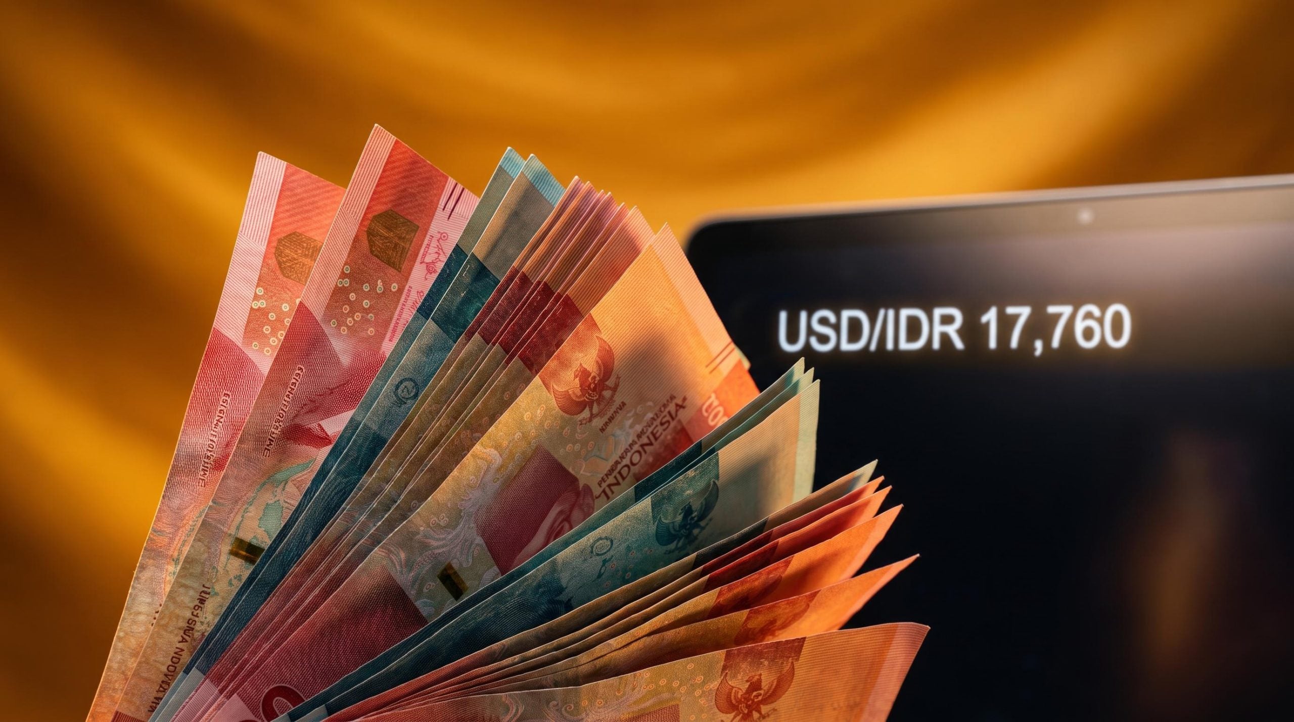 Indonesian Rupiah banknotes fanned upward with USD/IDR 17,760 on a trading screen — currency holds firm despite record deficit