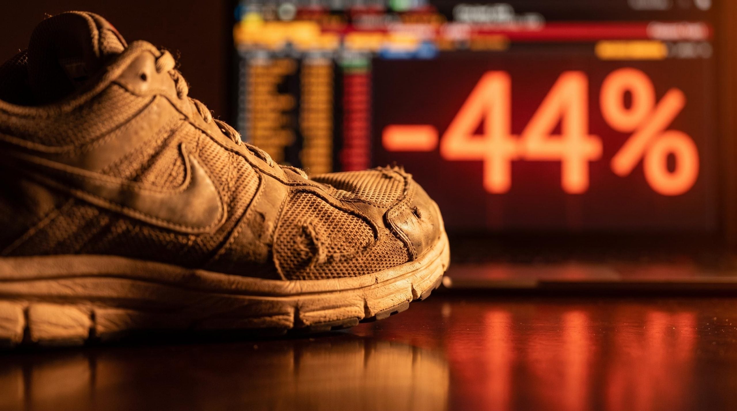 Nike shoe on trading floor surface with -44% stock decline data glowing in amber behind it